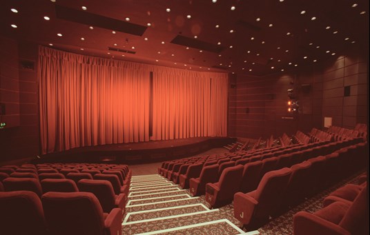 A large empty cinema with red curtains and seats.
